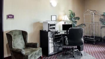 A hotel room with a vintage armchair, a desk with a printer, a computer, and a metal cart.