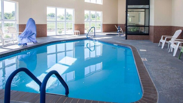 Una piscina interior con paredes de vidrio transparente, suelo de baldosas y algunas sillas de descanso.