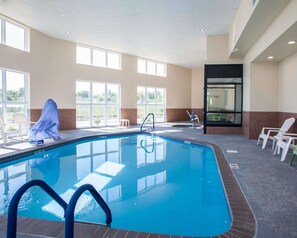 Une piscine intérieure avec des parois en verre transparent, un sol carrelé et quelques chaises longues.
