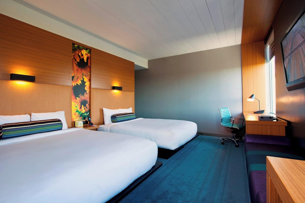 A hotel room with two beds, a desk, a chair, and a large window.