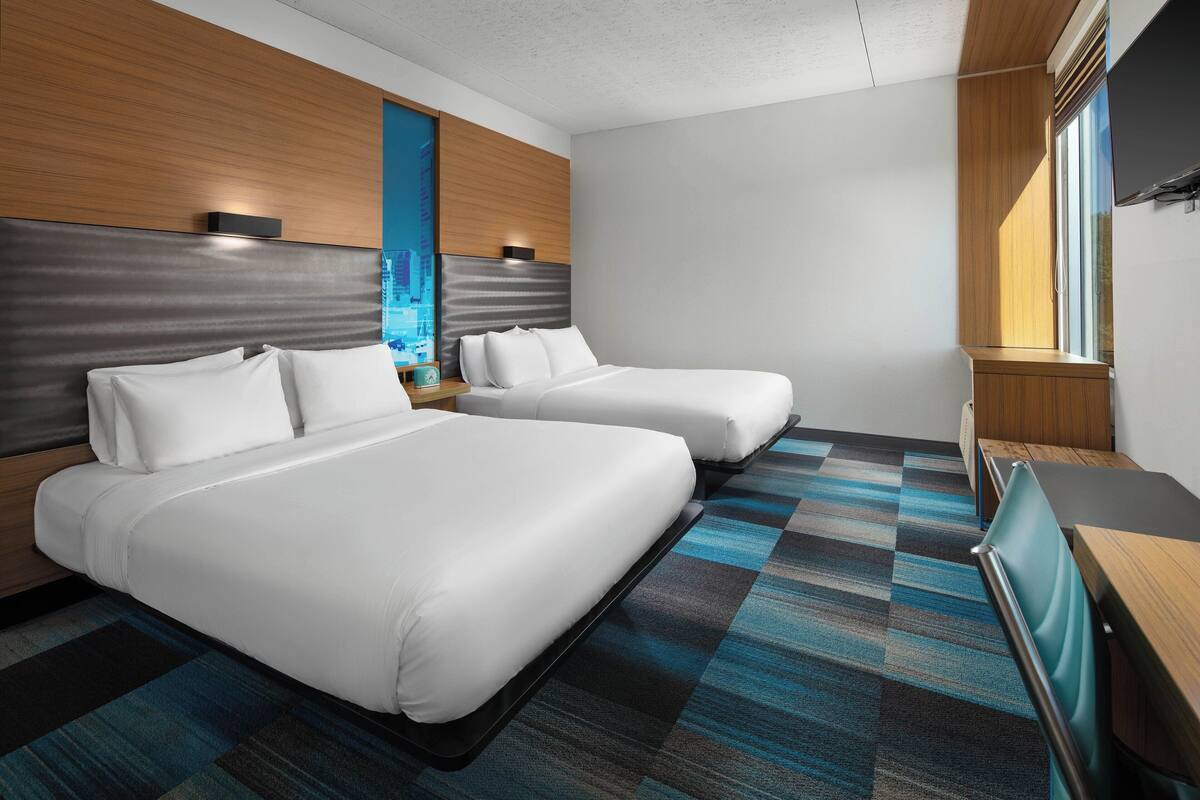 A hotel room with two beds, a wooden headboard, a blue and black striped carpet, and a TV on a wooden table.