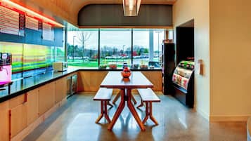 A modern cafe with a wooden table and benches, a menu board, and a view of a parking lot through large windows.