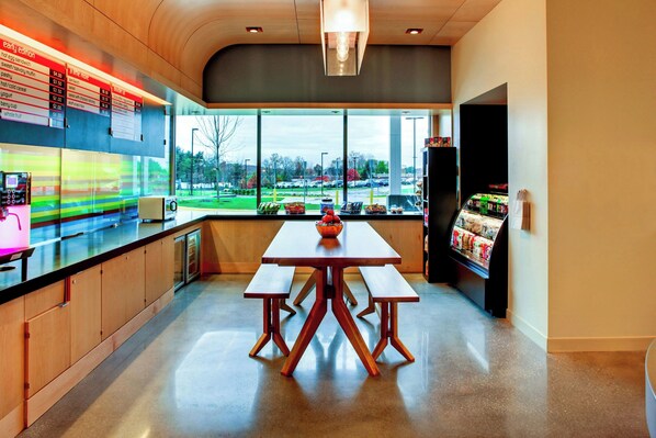 Un café moderno con una mesa y bancos de madera, un tablero de menú y vistas a un estacionamiento a través de amplios ventanales.