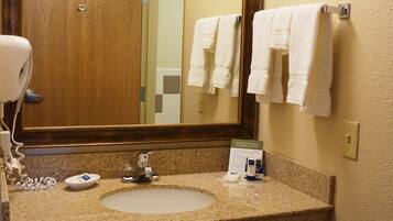 A bathroom with a granite countertop, a sink, a mirror, a hairdryer, and a trash can.