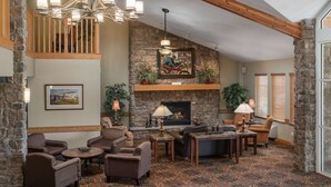 A cozy living room with a stone fireplace, comfortable seating, and a decorative ceiling light. - AmericInn by Wyndham Anamosa (Anamosa)