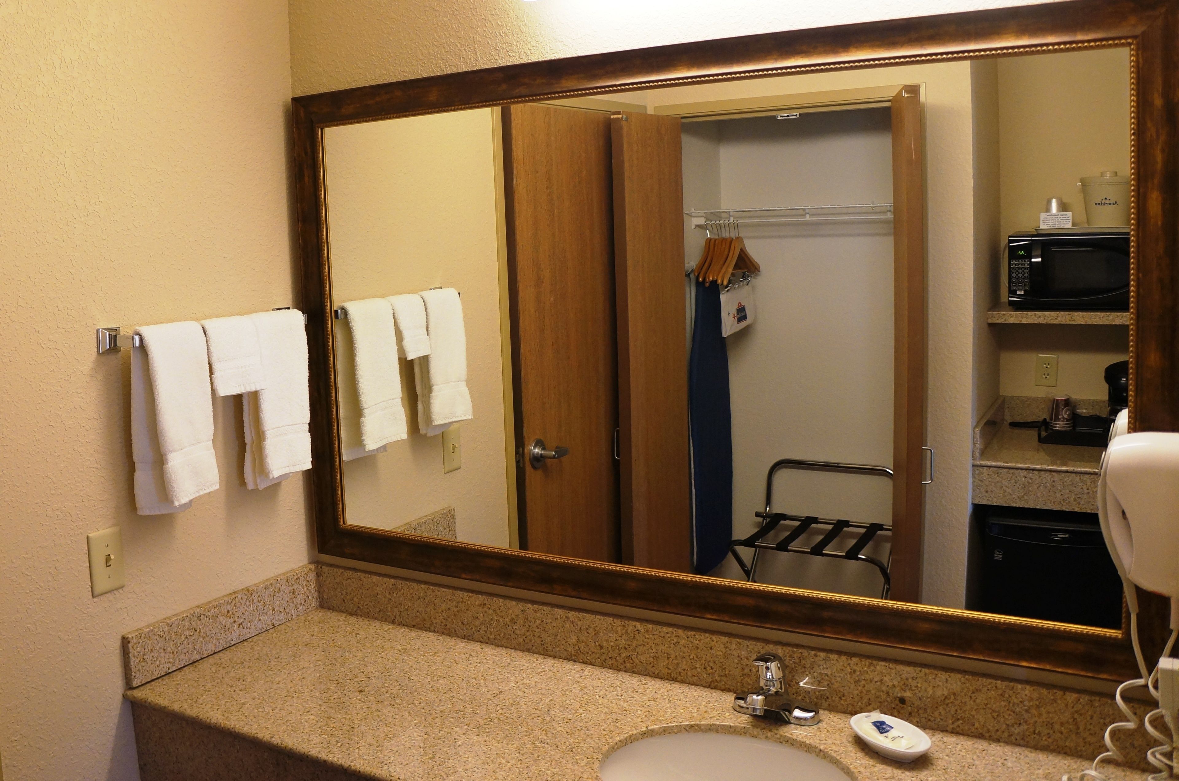 A bathroom with a large mirror, a sink, a towel rack with towels, a shower curtain, a hairdryer, and a microwave.