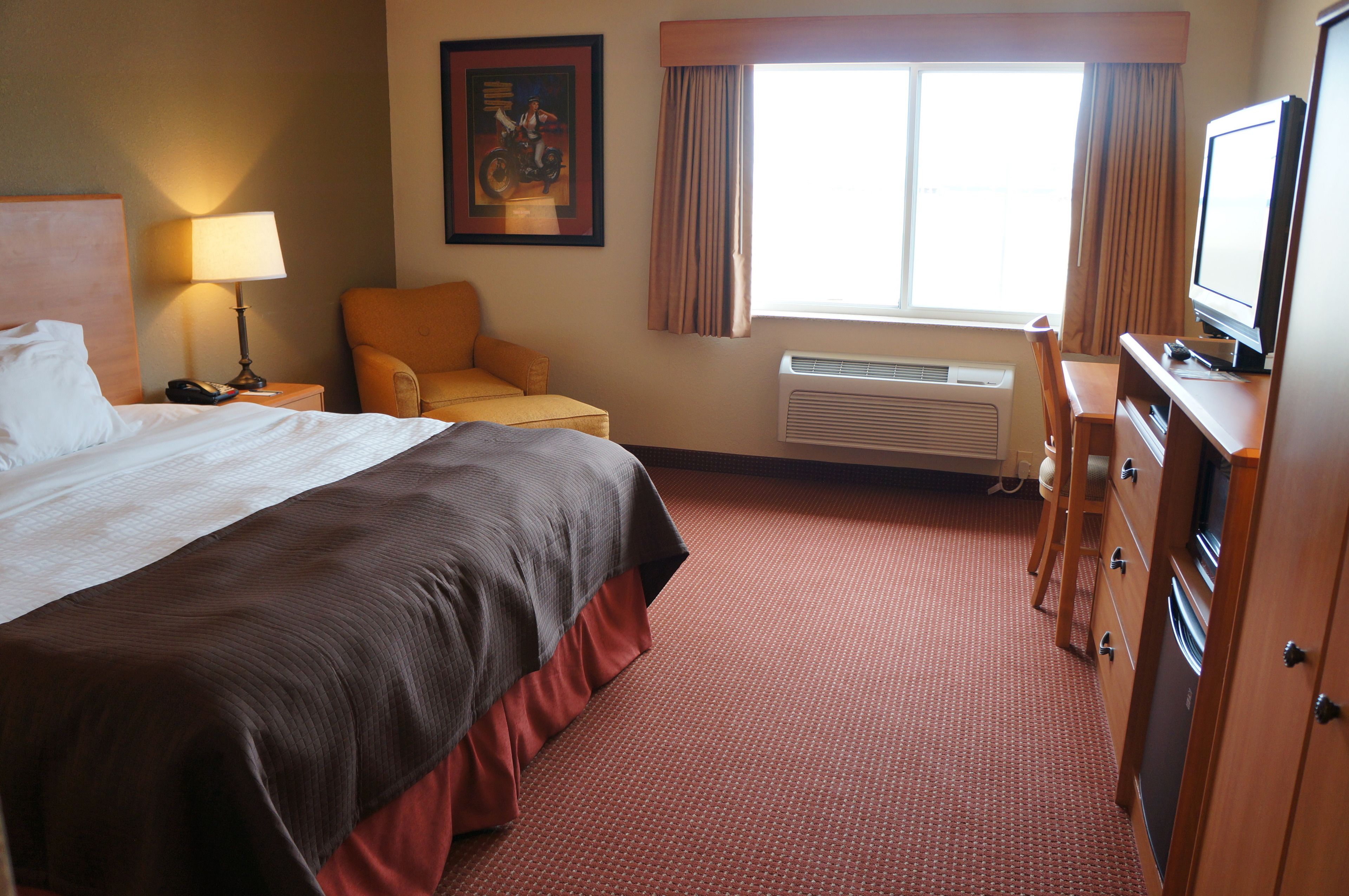 A hotel room with a large bed, a desk, a chair, a television, and a window with curtains.