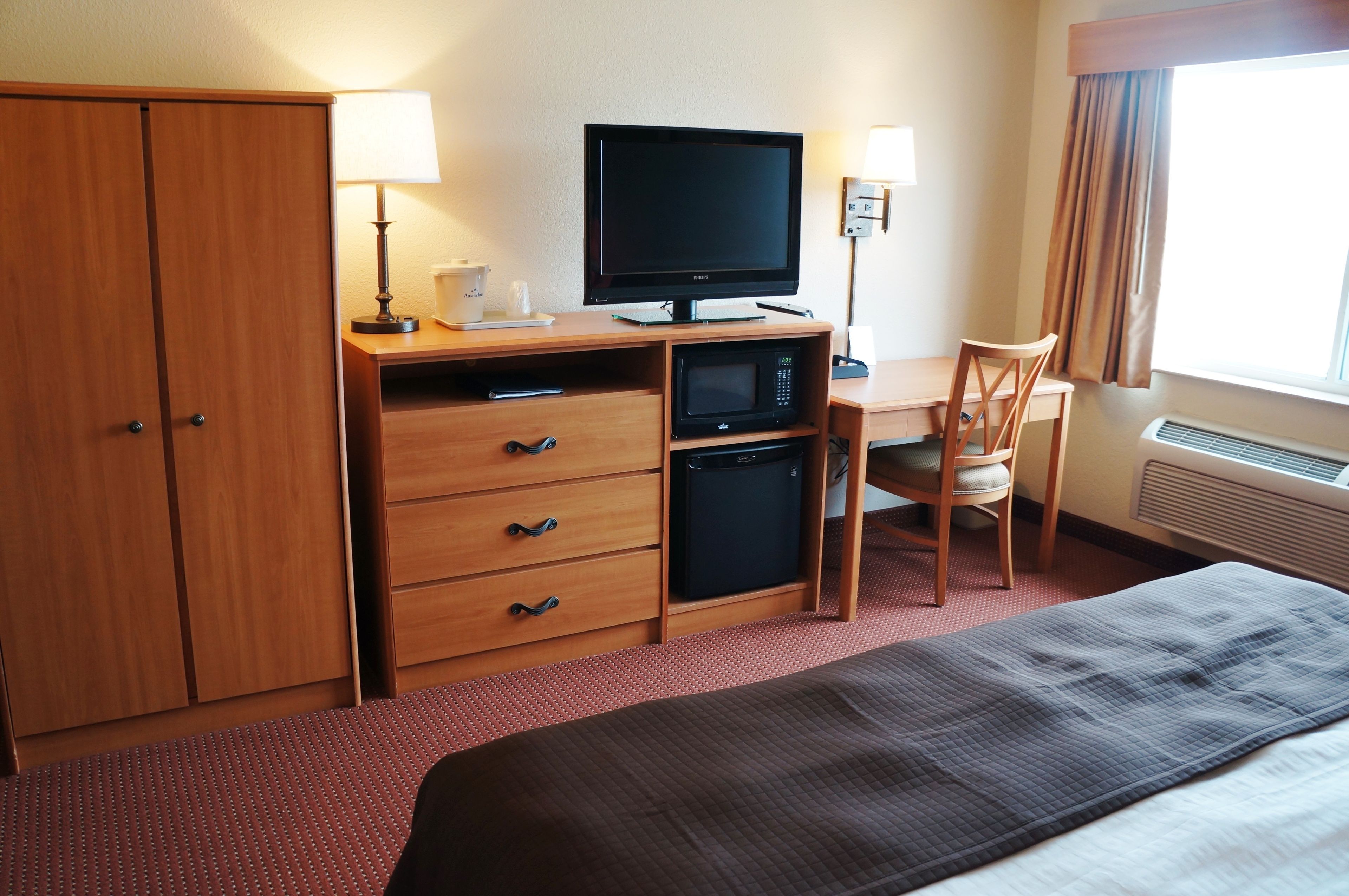 A hotel room with a bed, a desk with a computer, a television, a microwave, a chair, and a wardrobe.