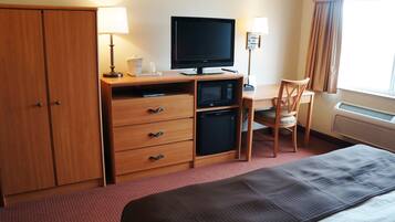 A hotel room with a bed, a desk with a computer, a television, a microwave, a chair, and a wardrobe.