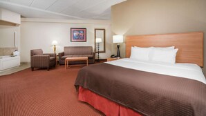 A hotel room with a large bed, a sitting area with two chairs, a small table, a lamp, and a painting on the wall. - AmericInn by Wyndham Anamosa (Anamosa)