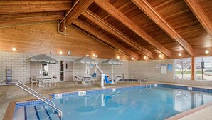 An indoor swimming pool with wooden beams, tiled walls, and a seating area with umbrellas. - AmericInn by Wyndham Anamosa (Anamosa)