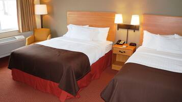 Quarto de hotel com duas camas, uma cadeira, mesa de cabeceira com abajur e janela com cortinas.
