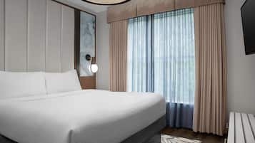 Una habitación de hotel moderna con una cama grande, una mesita de noche, una lámpara de pared y una ventana con cortinas.