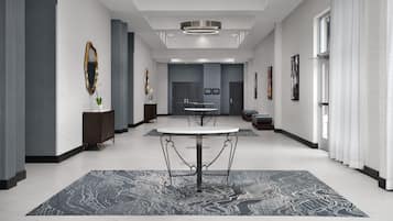 A spacious hotel lobby with a central round table, a patterned rug, and modern decor.