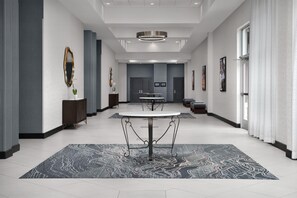A spacious hotel lobby with a central round table, a patterned rug, and modern decor.