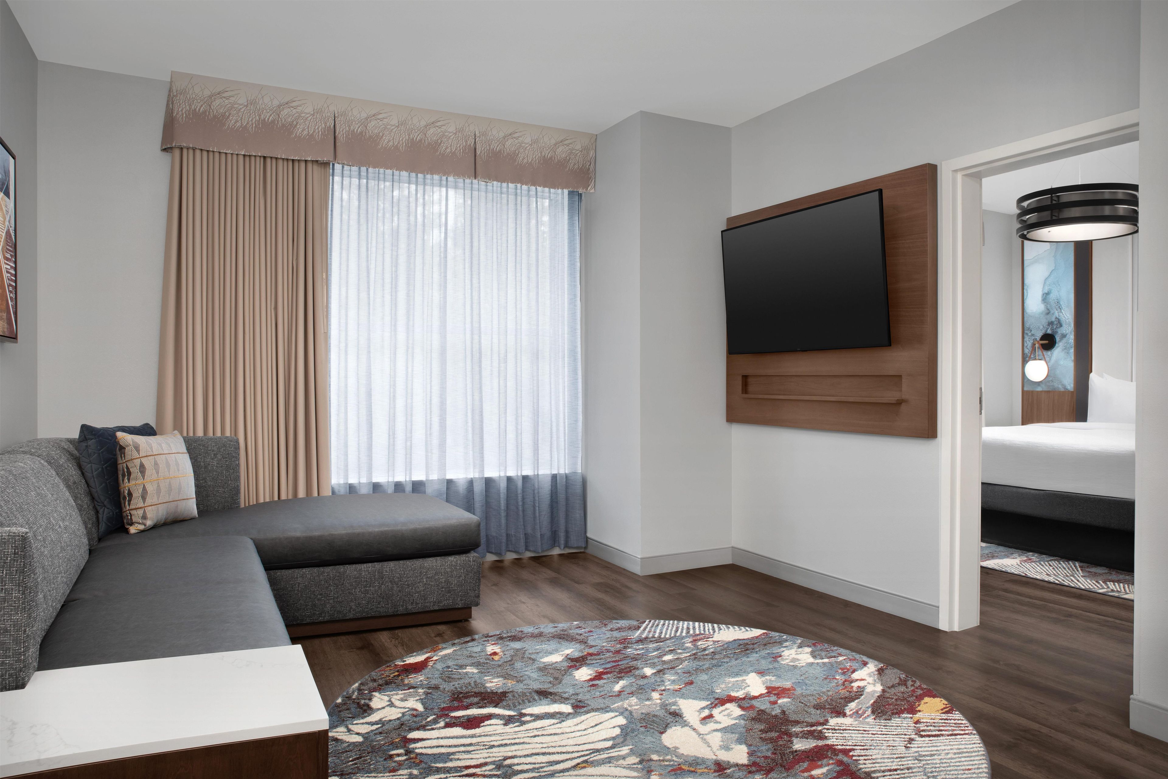 A modern living room with a sectional sofa, a flat-screen TV mounted on the wall, and a patterned rug on the floor.