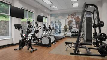 A gym with exercise equipment, large windows, and a mural.