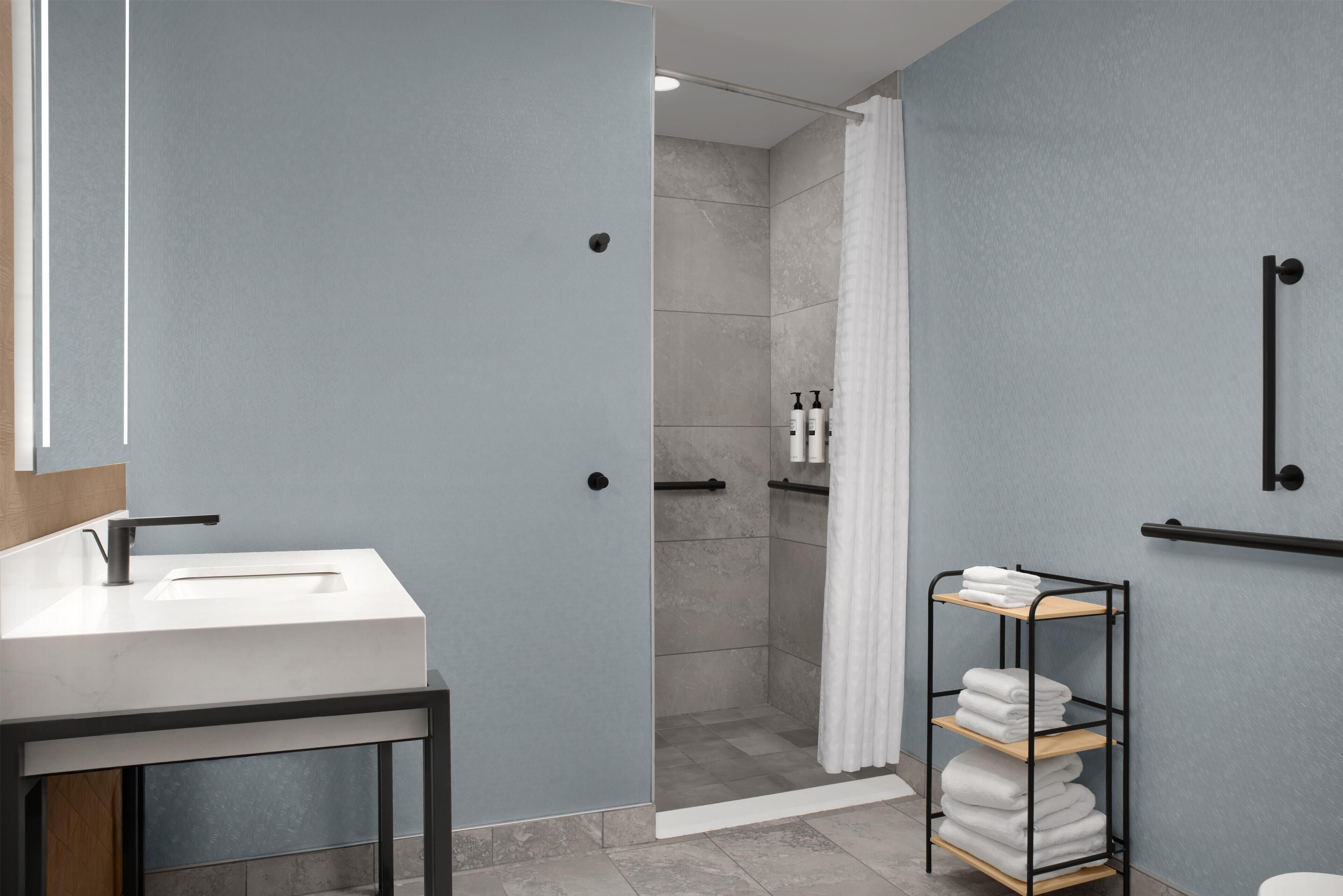 A modern bathroom with a shower, a sink, and a towel rack.