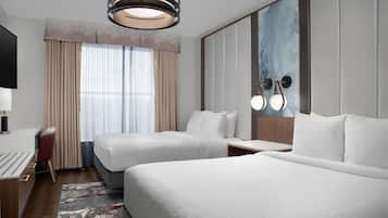 A hotel room with two beds, a desk, a chair, a TV, and a large window with curtains.