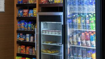 A vending machine with snacks and drinks, located in a room with wooden cabinets and tiled flooring.