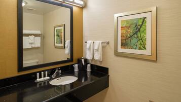 Une salle de bain d’hôtel avec un lavabo à vasque sur un plan de toilette noir, un grand miroir et deux œuvres d’art encadrées accrochées au mur.