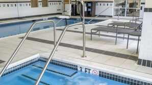 Ein Hallenbad mit Whirlpool, Metallleitern und gefliestem Boden.
