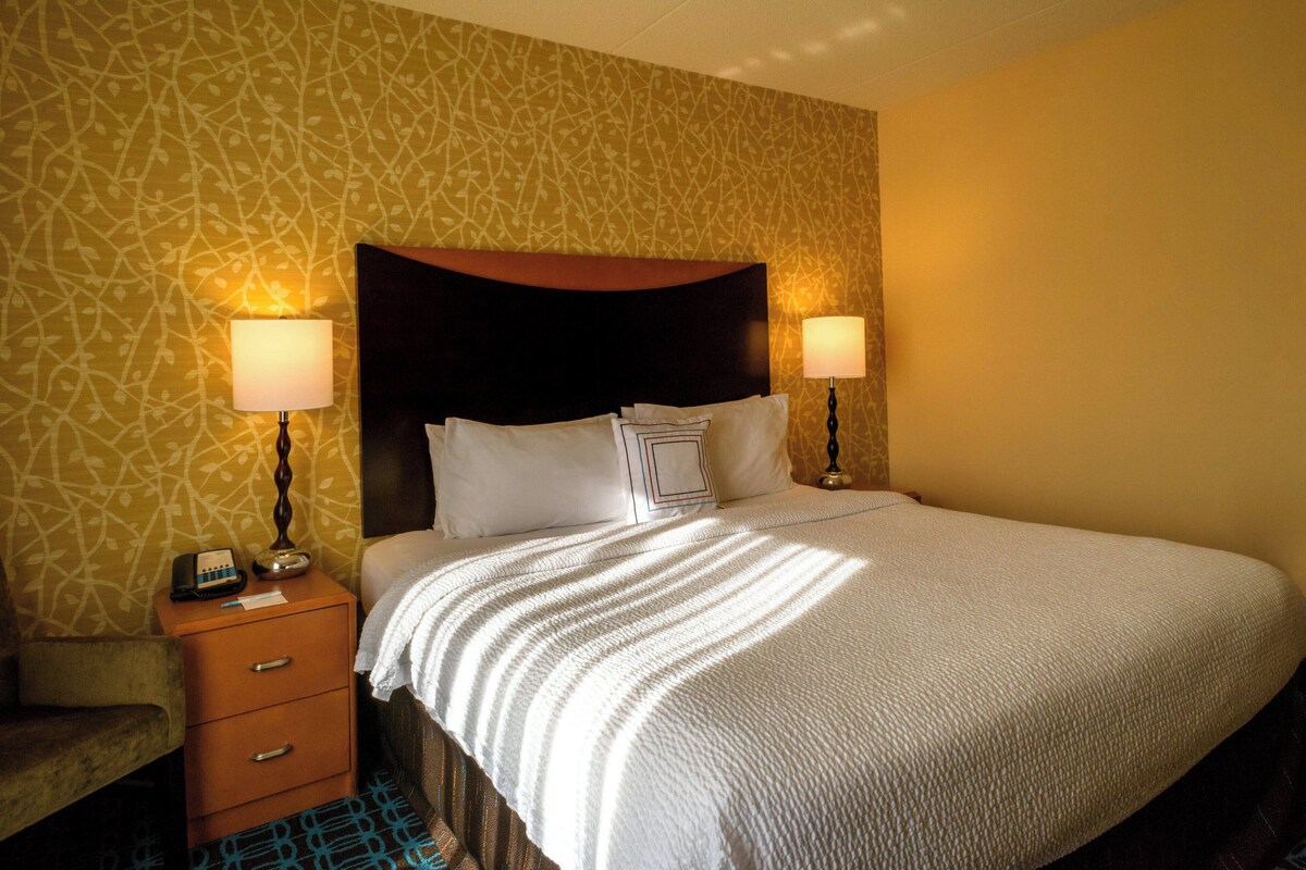 A hotel room with a bed, two bedside lamps, a nightstand, and a patterned wallpaper.