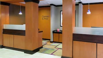 Un'area reception con scrivanie in legno, un cartello con la scritta 'Connect & Print' e una moquette a motivi.