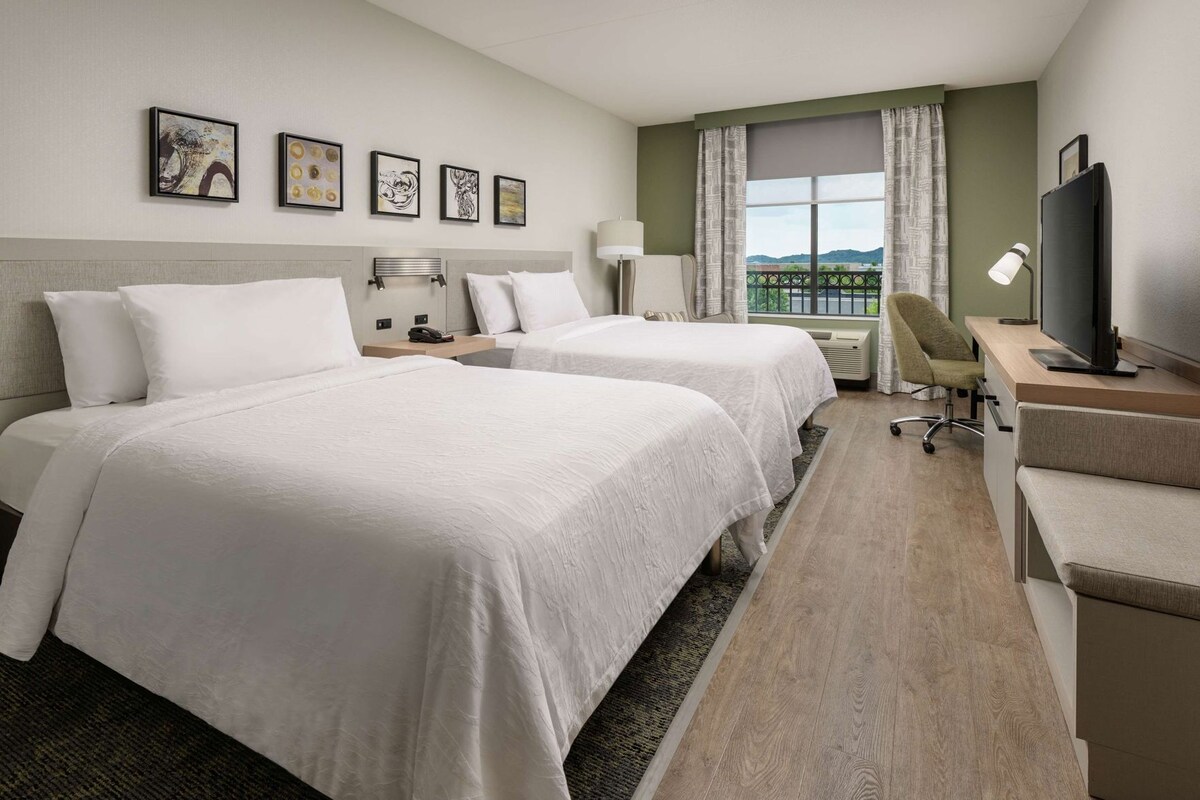 A hotel room with two beds, a desk with a computer, a TV, and a window with a view.