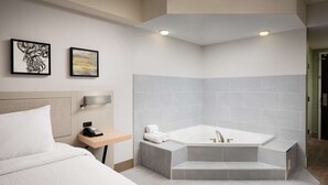 Una habitación de hotel moderna con una cama grande, una bañera en esquina y dos obras de arte enmarcadas en la pared.