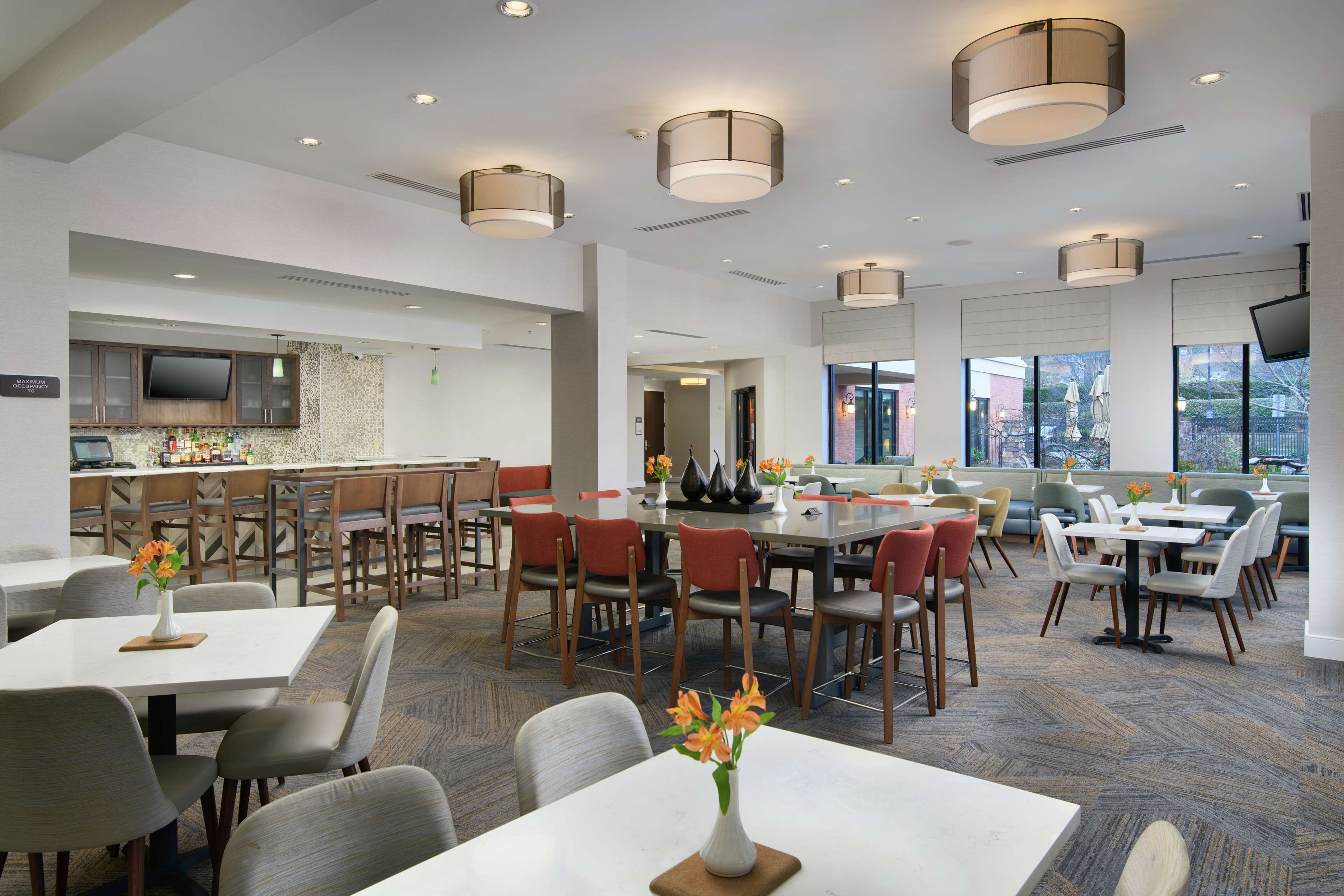 A modern hotel lobby with multiple seating areas, a bar, and a television.