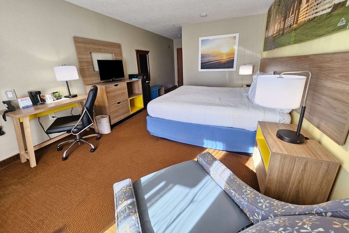 Een hotelkamer met een bed, bureau, stoel en een schilderij aan de muur.