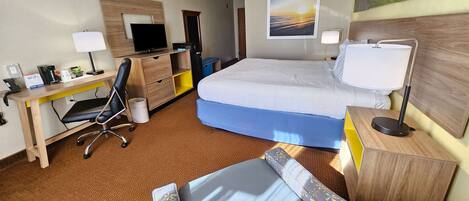 A hotel room with a bed, desk, chair, and a painting on the wall.