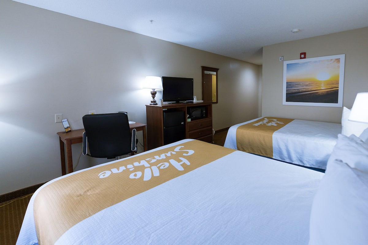 Een hotelkamer met twee bedden, een bureau, een televisie en een schilderij aan de muur.