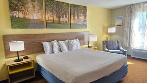 A hotel room with a large bed, a nightstand with a lamp, a chair, and a painting on the wall. - Days Inn by Wyndham Greensboro NC (Greensboro)