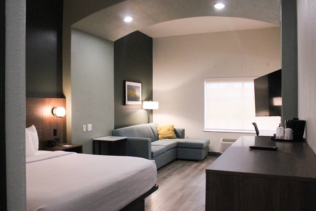 A modern hotel room with a bed, a sofa, a desk, and a large window.