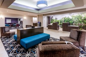 A modern hotel lobby with a reception desk, seating area with sofas and armchairs, a coffee machine, and a large window offering a view of greenery. - La Quinta Inn & Suites by Wyndham Lumberton (Lumberton)