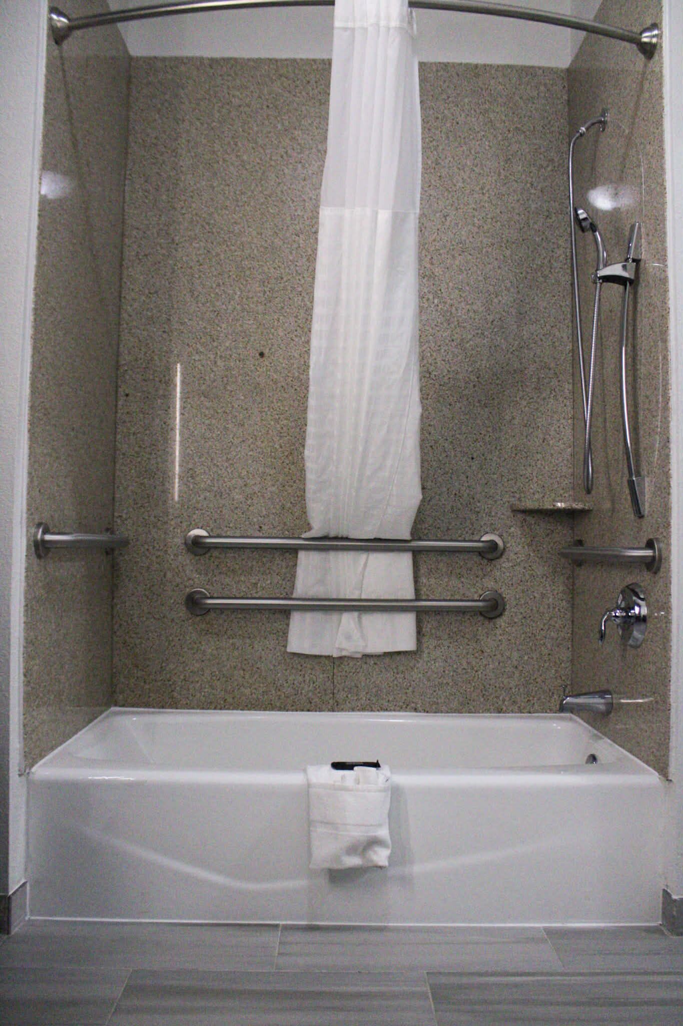 A modern bathroom with a bathtub, shower, and grab bars.
