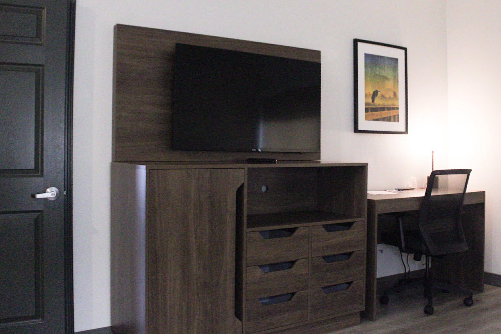 Une pièce avec un meuble en bois foncé, un téléviseur à écran plat fixé au mur, un bureau avec une chaise et un tableau encadré accroché au mur.