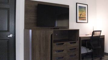 Una habitación con un mueble de madera oscura, un televisor de pantalla plana montado, un escritorio con una silla y un cuadro en la pared.
