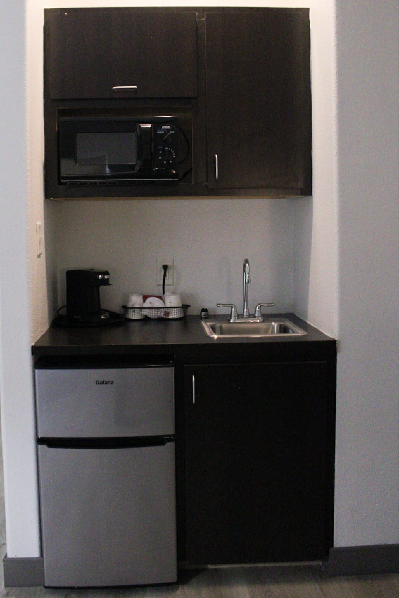 A compact kitchen with a built-in microwave, a coffee maker, a sink, and a refrigerator.