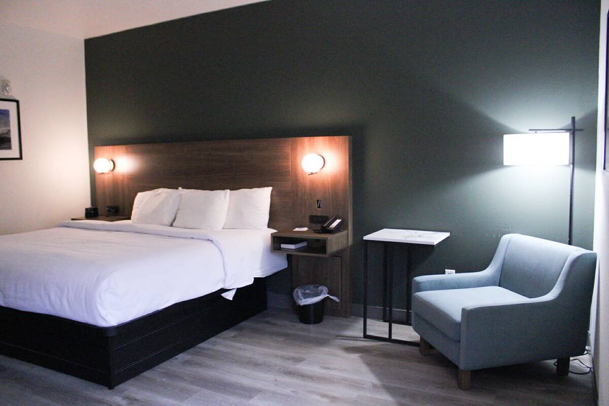 A hotel room with a large bed, bedside tables, a chair, and a wall-mounted light fixture.