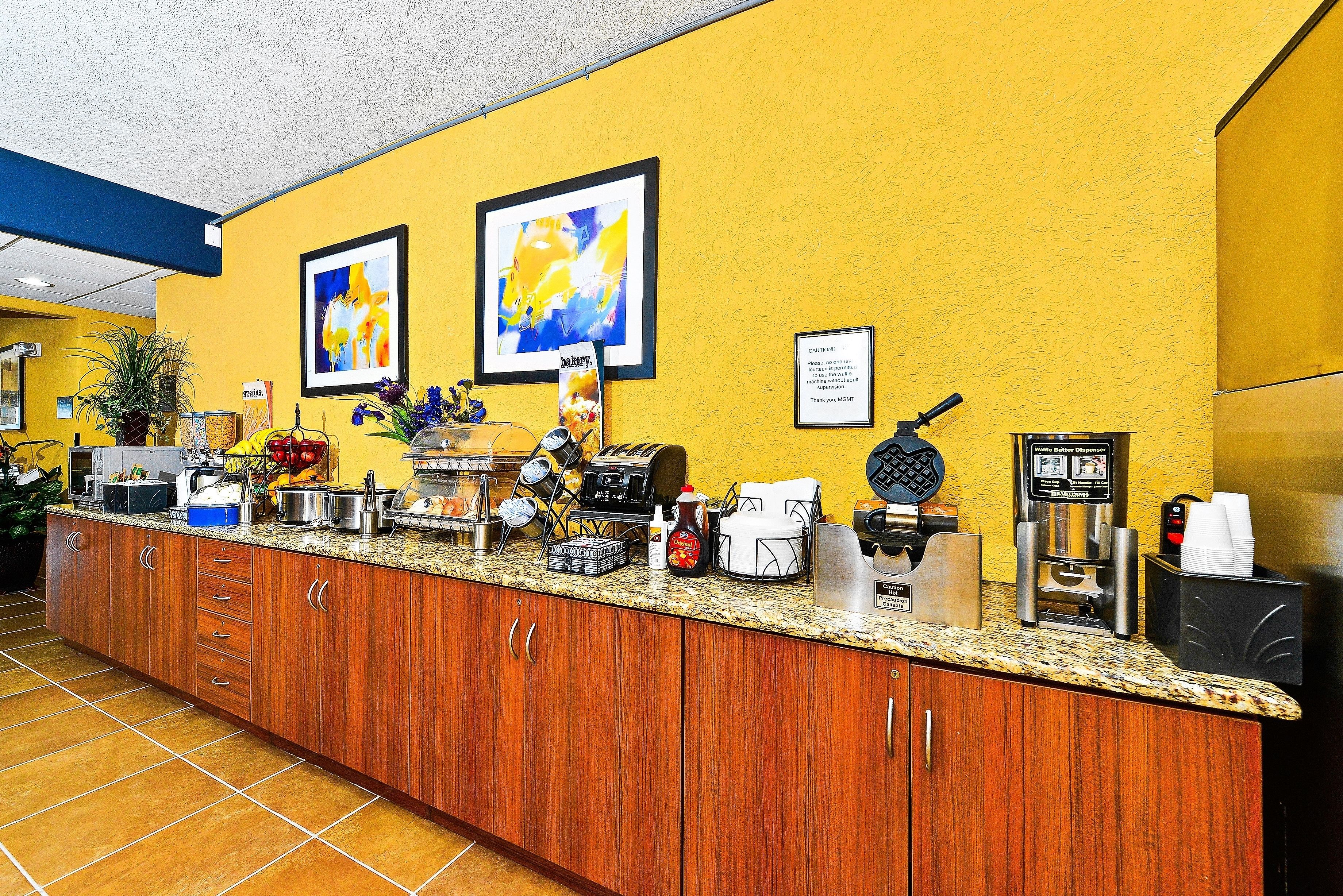 Zona de recepción de hotel con mostrador de madera, máquinas de café y cuadros en la pared.