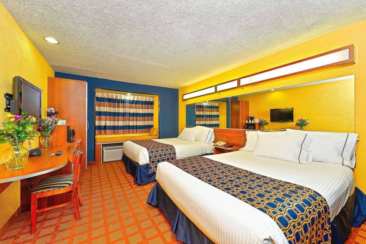 A hotel room with two beds, a desk, a chair, a television, and a window with curtains.