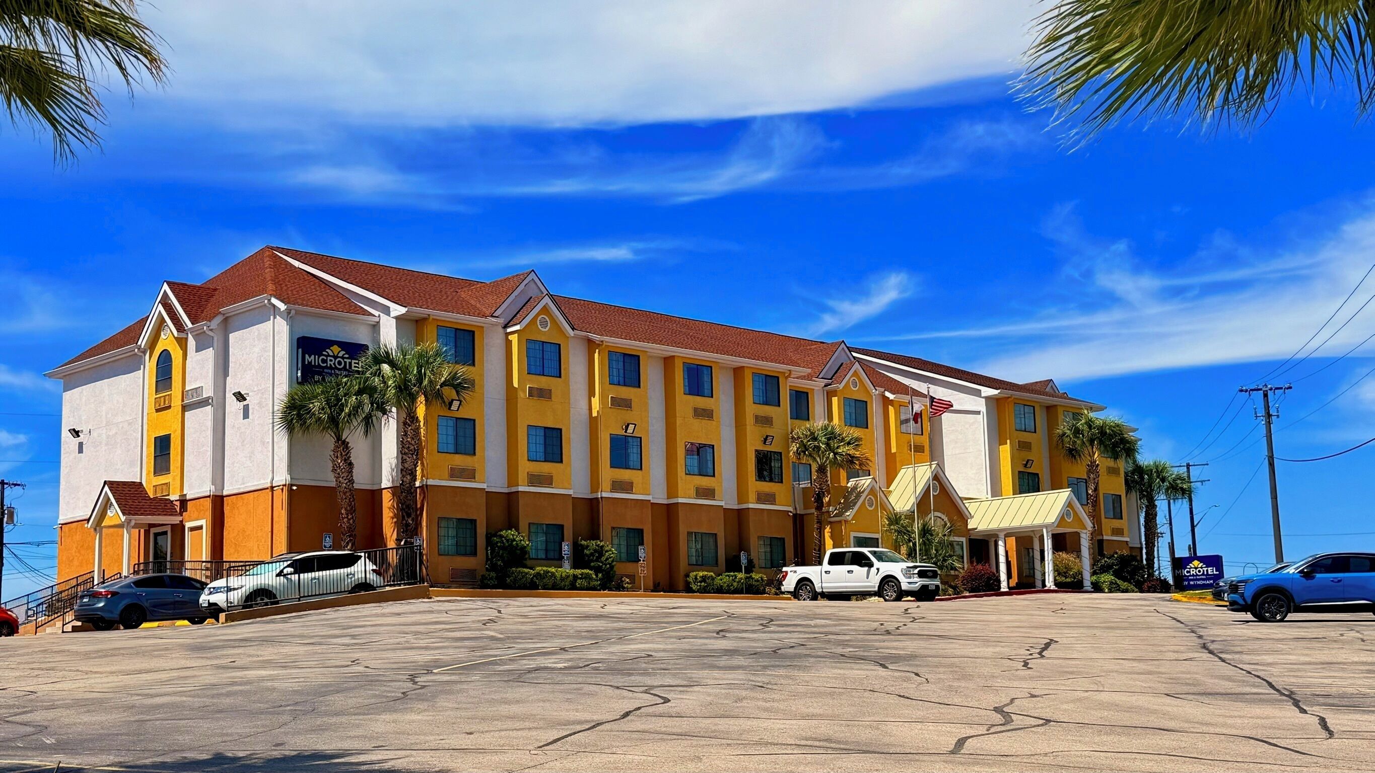 A multi-story hotel with a red roof and yellow and white exterior walls, featuring a parking lot with several cars.
