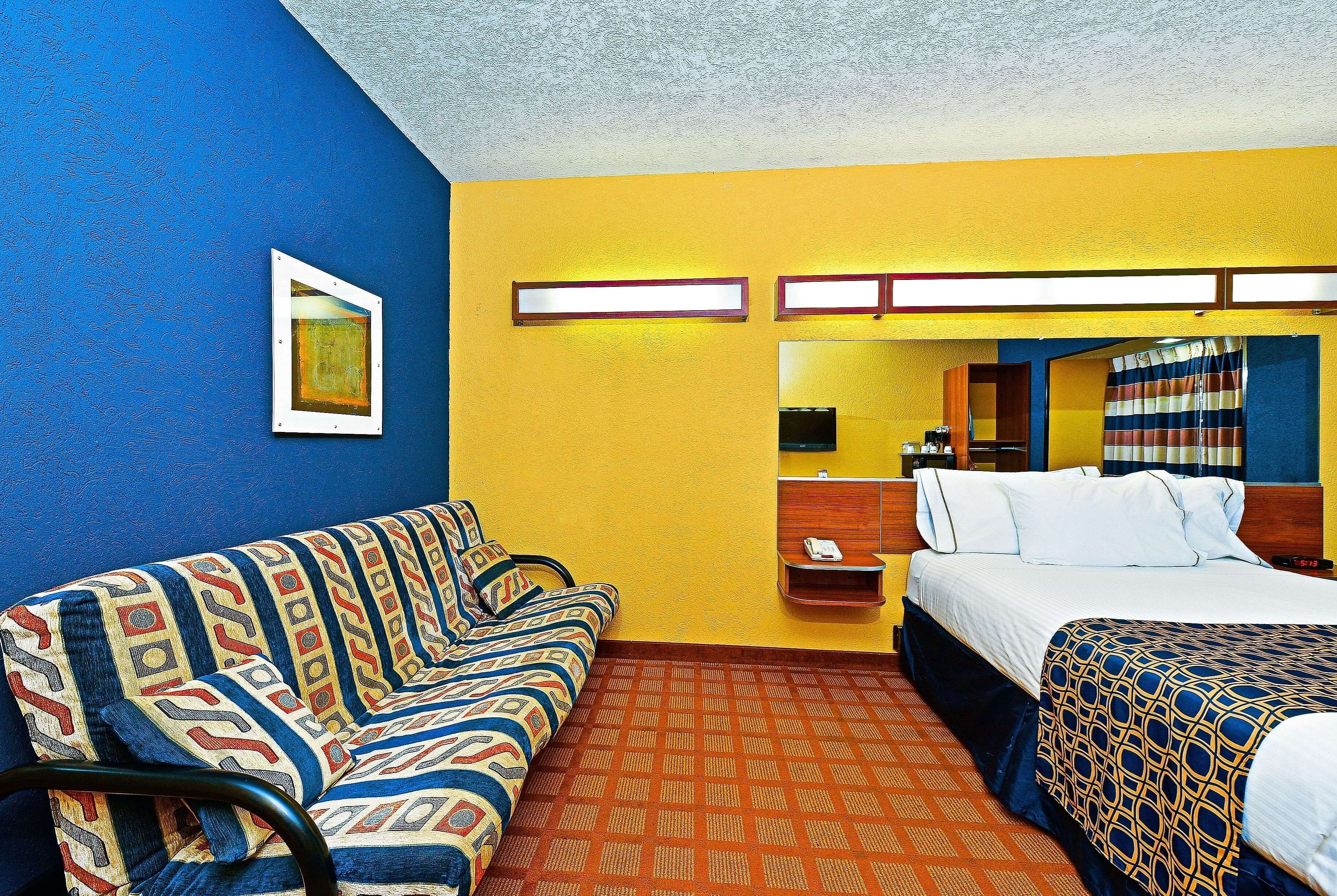 A hotel room with a patterned sofa, a bed with a patterned bedspread, a nightstand with a phone, and a mirror.