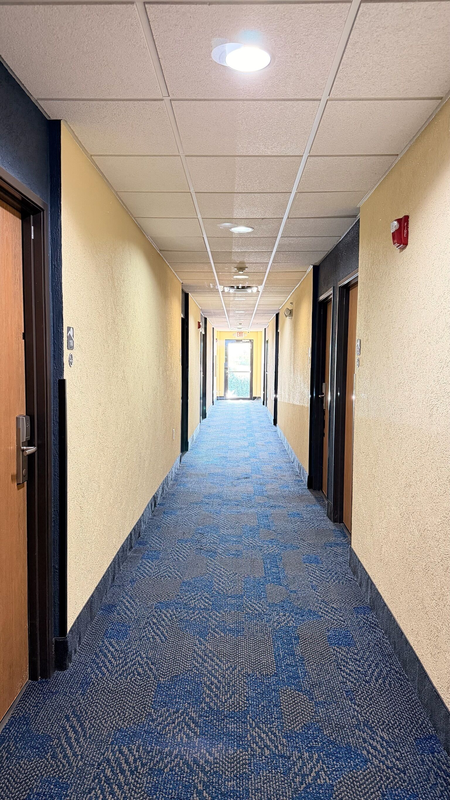 Corridoio di un hotel con pavimenti tappezzati, porte su entrambi i lati e soffitto con luci a incasso.