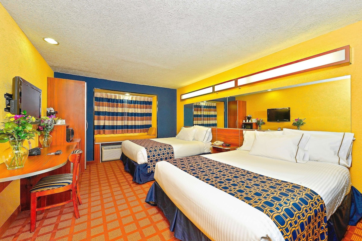 A hotel room with two beds, a desk with a chair, a mirror, and a television.