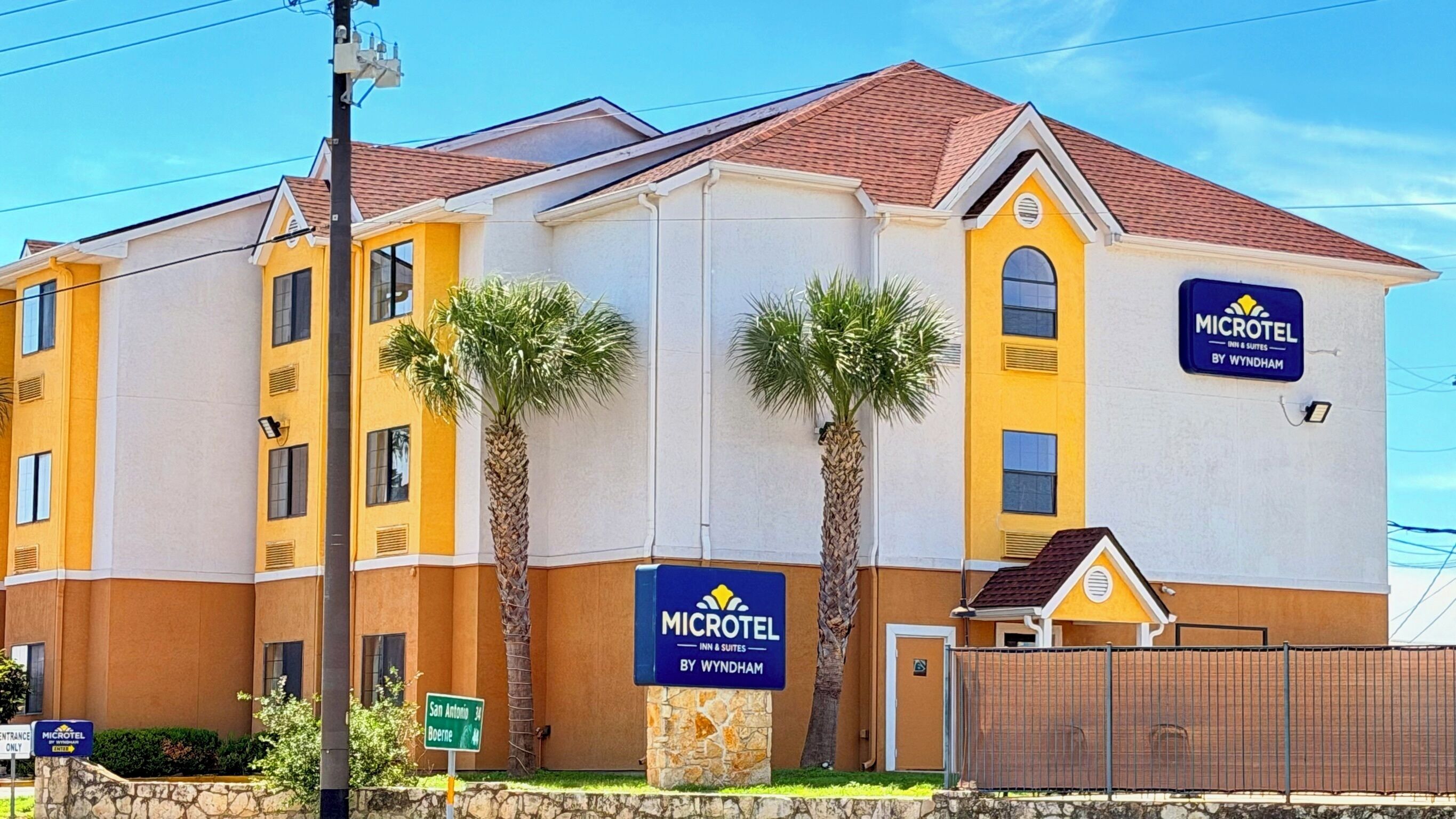 A Microtel Inn & Suites building with a yellow facade, palm trees, and a fenced parking area.