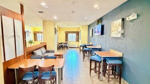 Un restaurante con cabinas, mesas altas y sillas. Hay luces en el techo y un televisor montado en la pared.